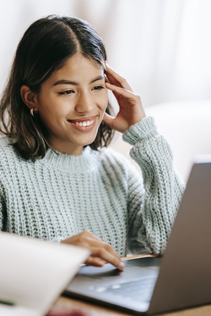 A young woman smiling as she uses a laptop to browse a website that has proper website maintenance services.