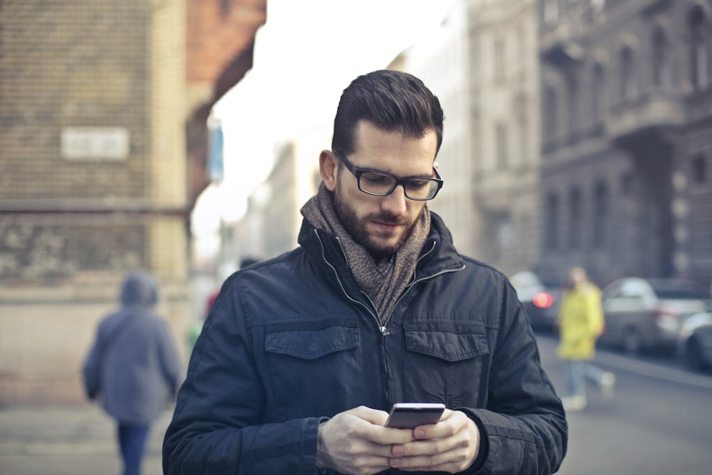 Adult man with glasses using a smartphone on a city street in Budapest, Hungary.
